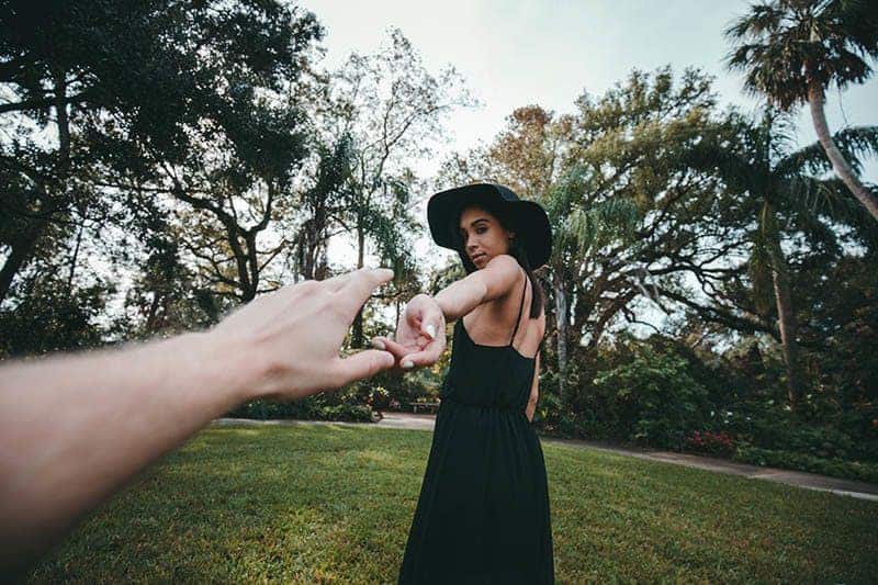 kvinna i svart klänning och hatt som håller handen