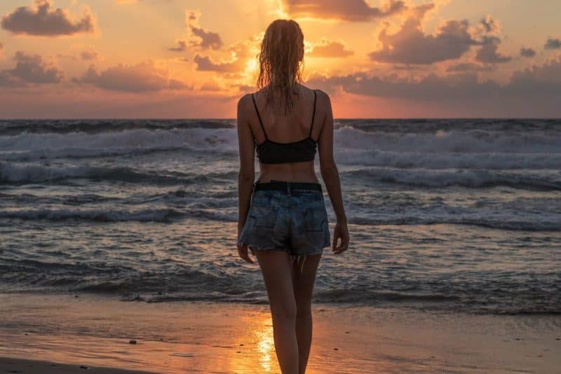 kvinna som står ensam på stranden i solnedgången