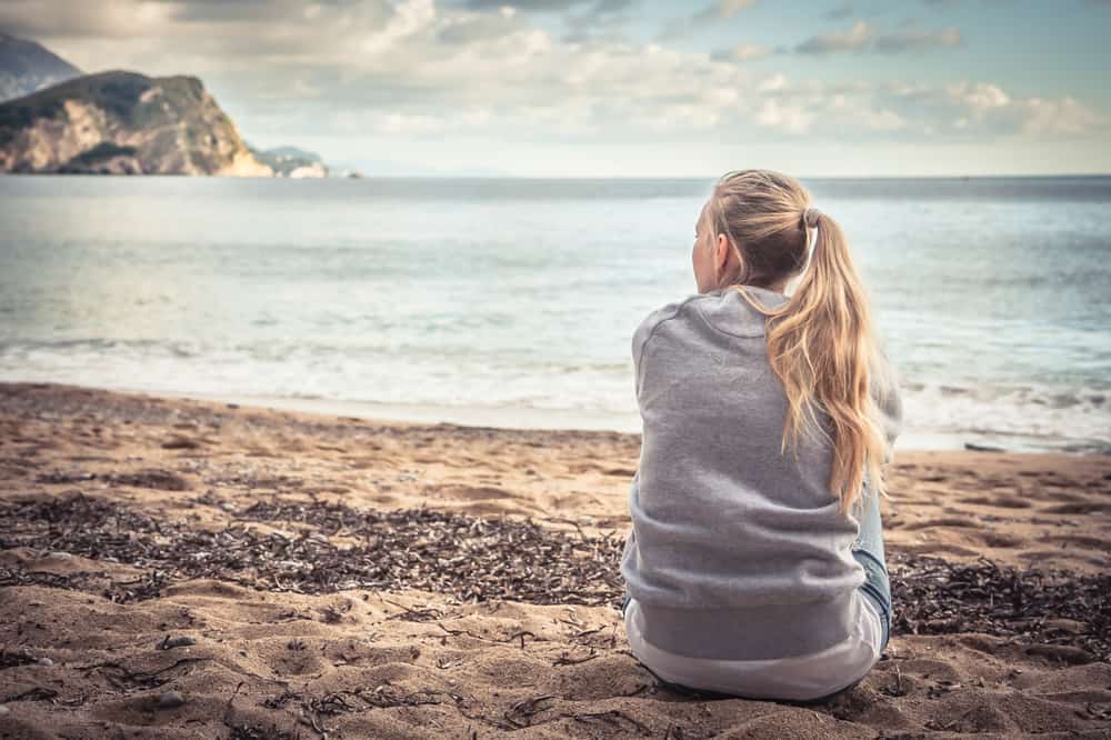 Eftertänksamt ensamt sammanträde för ung kvinna på stranden