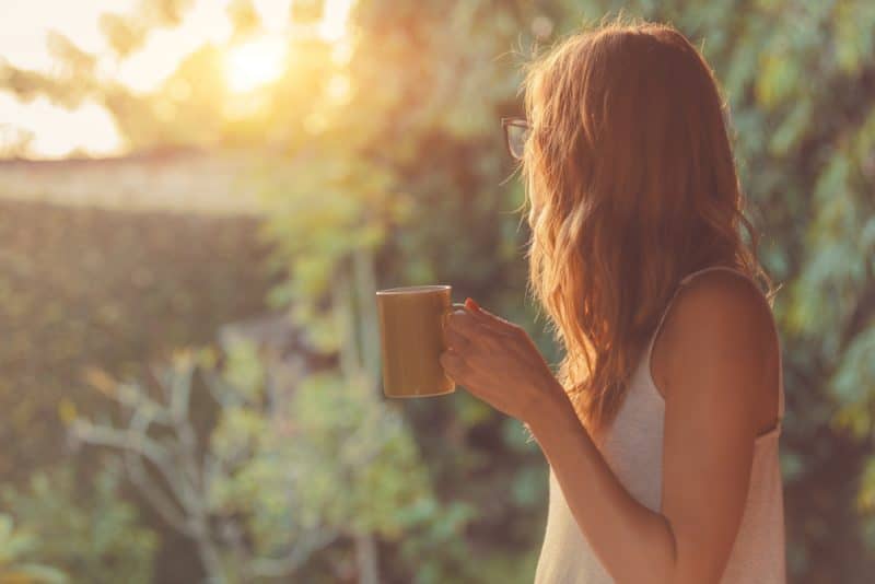 Söt flicka som tycker om morgonkaffe på verandan