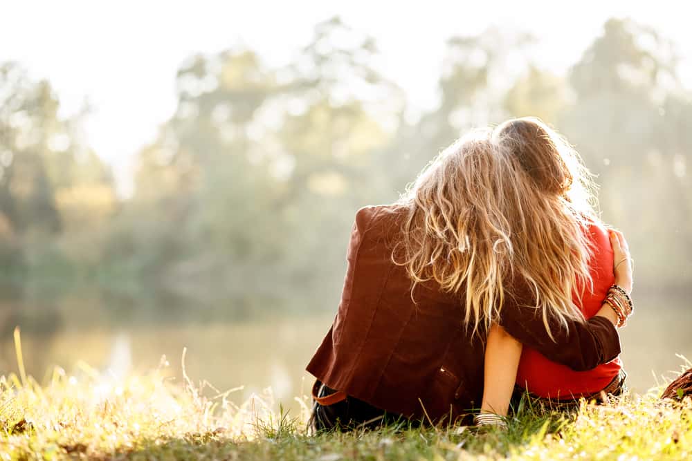 två kvinnor som sitter på gräset och kramar