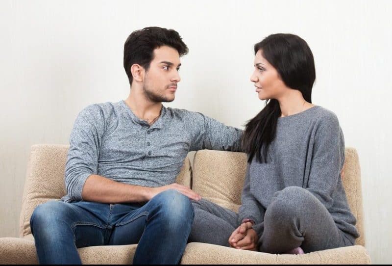 Unga lyckliga par som tillsammans talar sammanträde på en soffa