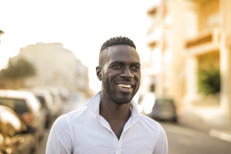 en leende svart man i en vit skjorta går ner på gatan