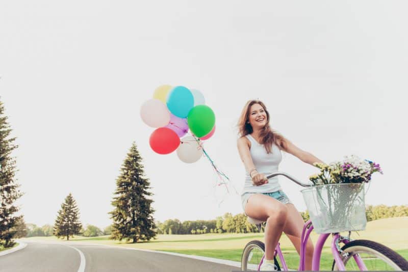 glad tjej som rider på en cykel med ballonger och ler