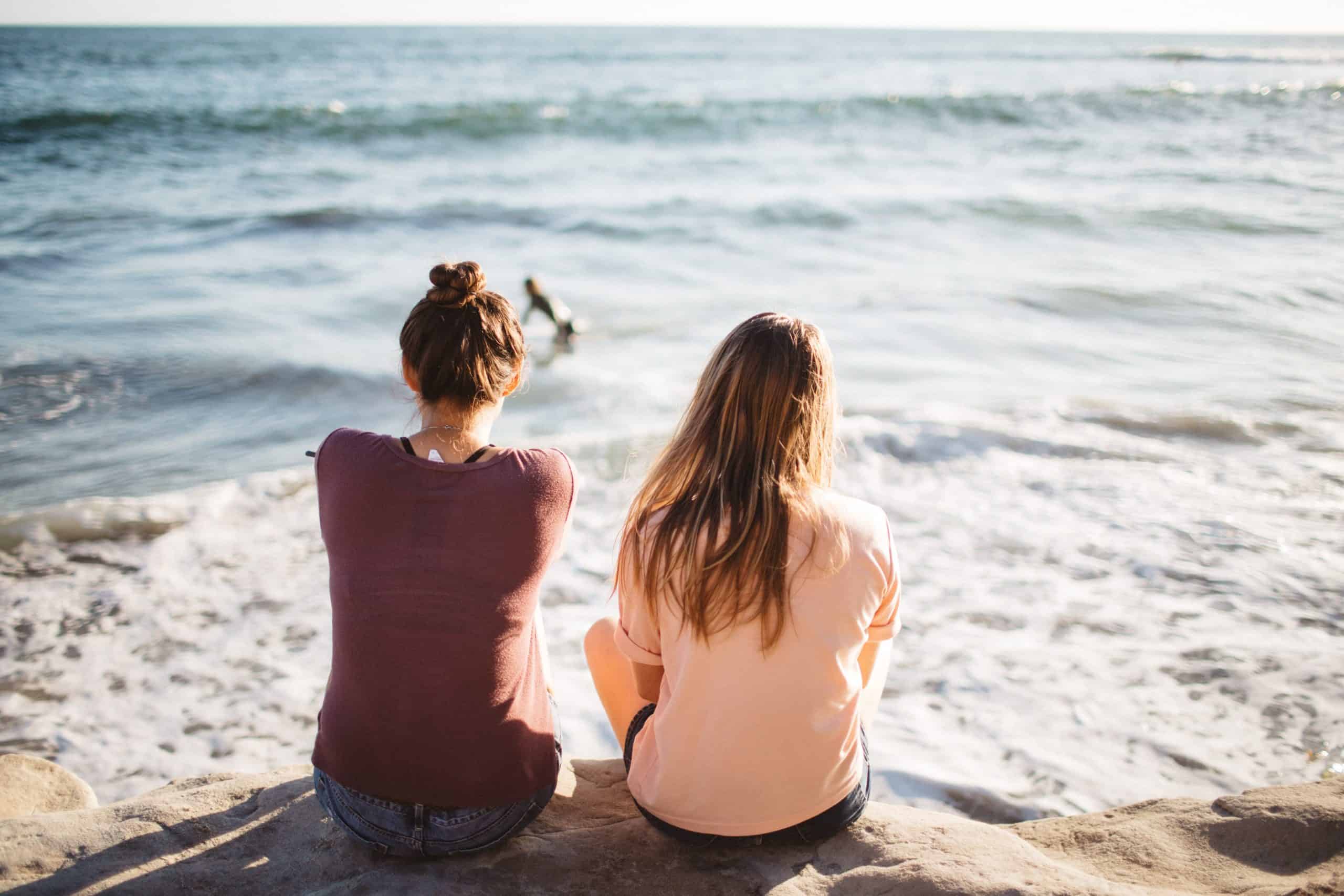 två kvinnor sitter tillsammans nära havet