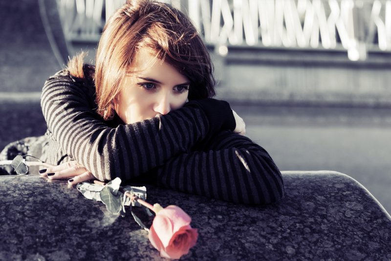 Ledsen ung kvinna med en röd ros