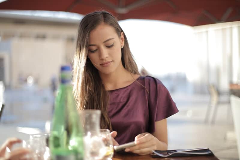 en kvinna i en lila klänning sitter på ett kafé och använder en mobiltelefon
