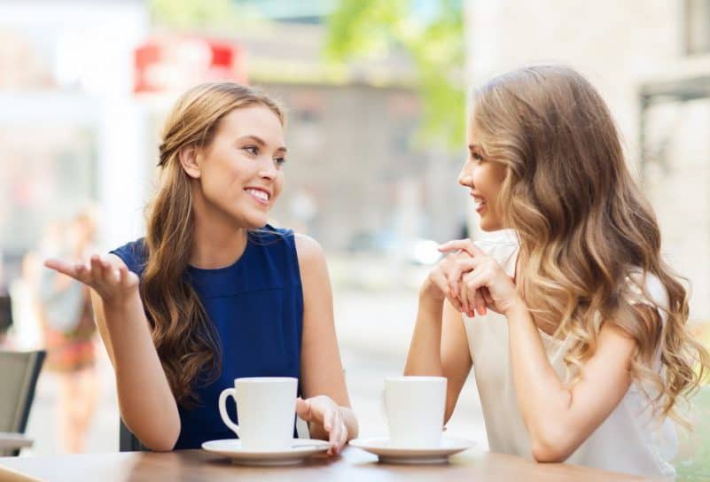 le unga kvinnor som dricker kaffe eller te och pratar på utomhuscafé