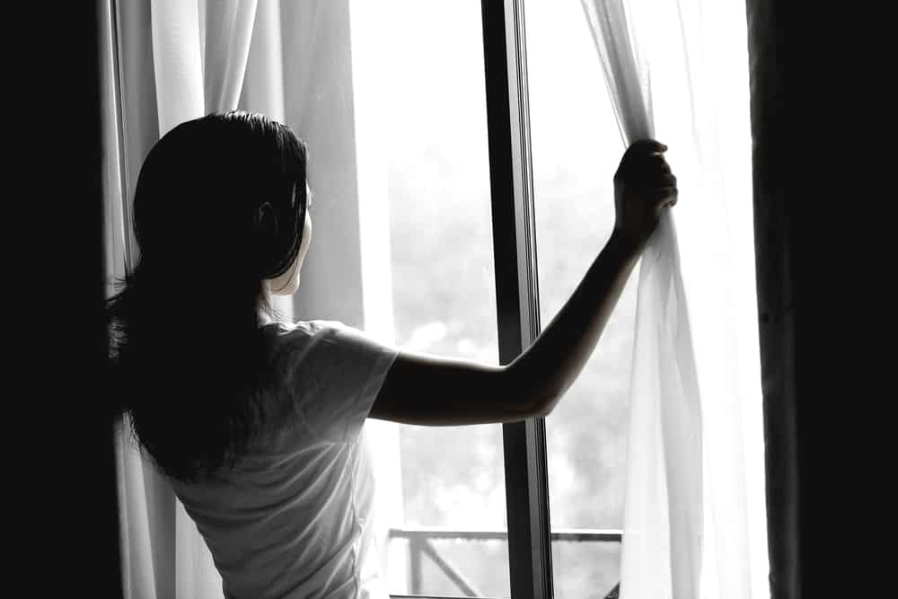 ung kvinna öppnar gardiner i ett sovrum