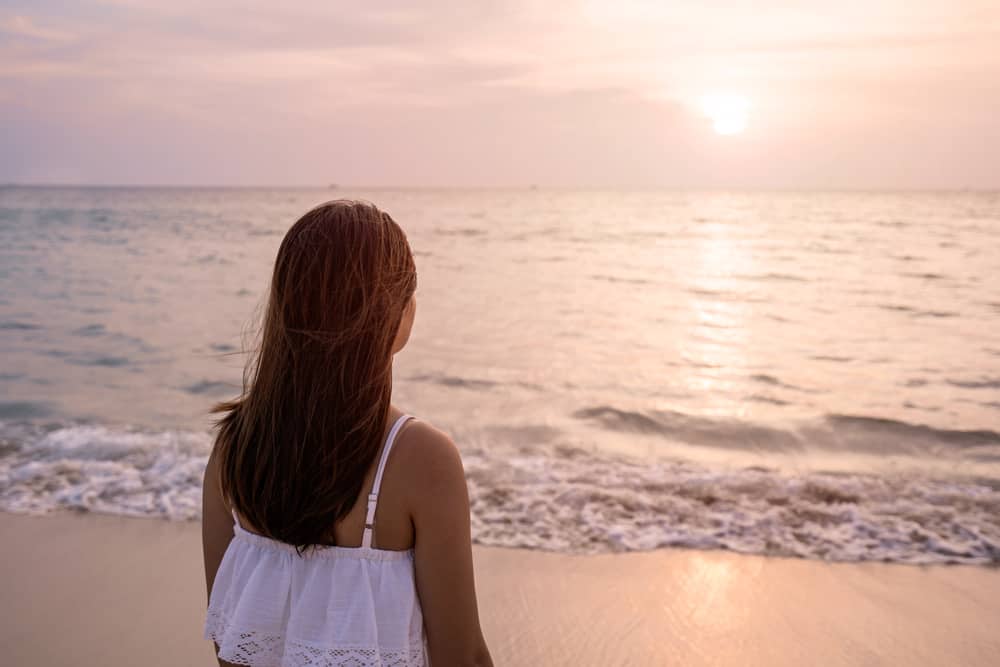ung kvinna som står på stranden ensam och ser solnedgången