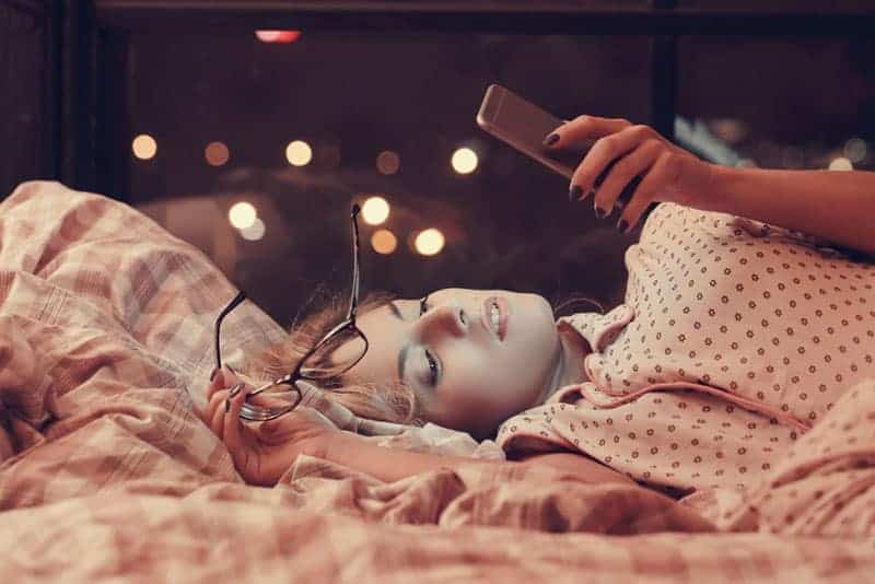 vacker ung kvinna som ligger på sängen och tittar på sin telefon