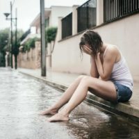 en sorglig kvinna sitter på trottoaren i regnet och gråter
