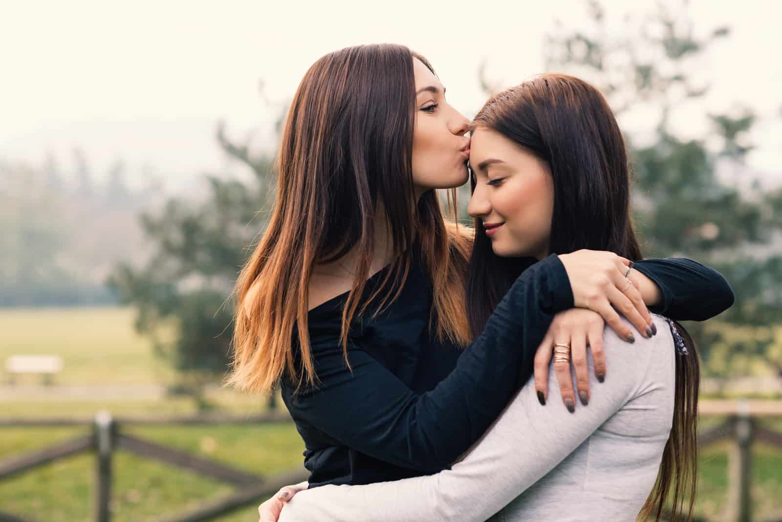 Stående av unga systrar som utomhus kramar och kysser i en parkera