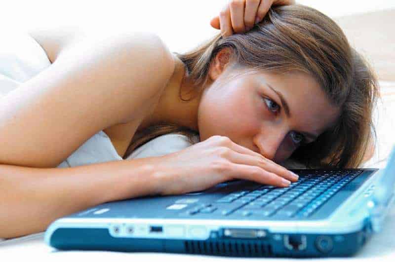 flicka som ligger i sängen och skriver på bärbar dator