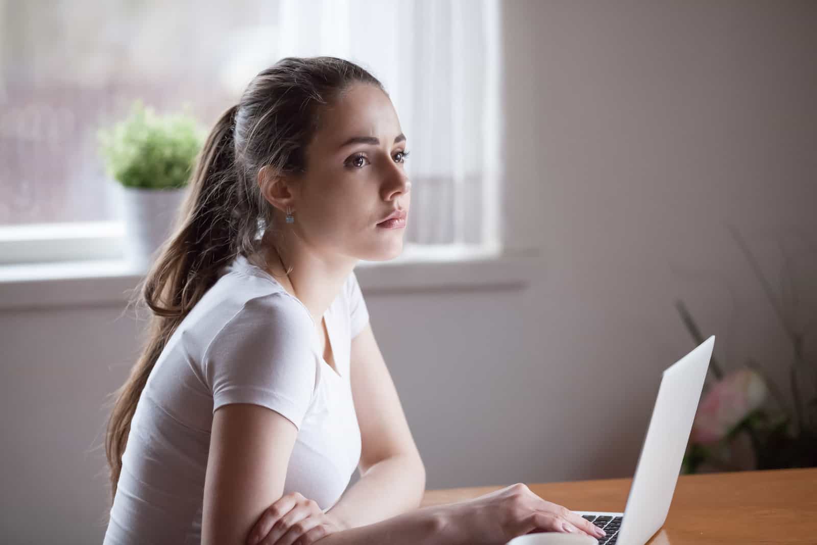 ganska ung kvinna som sitter vid bordet med bärbara datorn