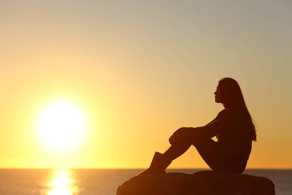 kvinna siluett titta på solen på stranden vid solnedgången