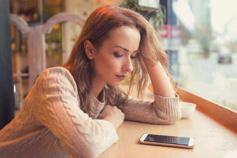 orolig kvinna som tittar på sin telefon i café