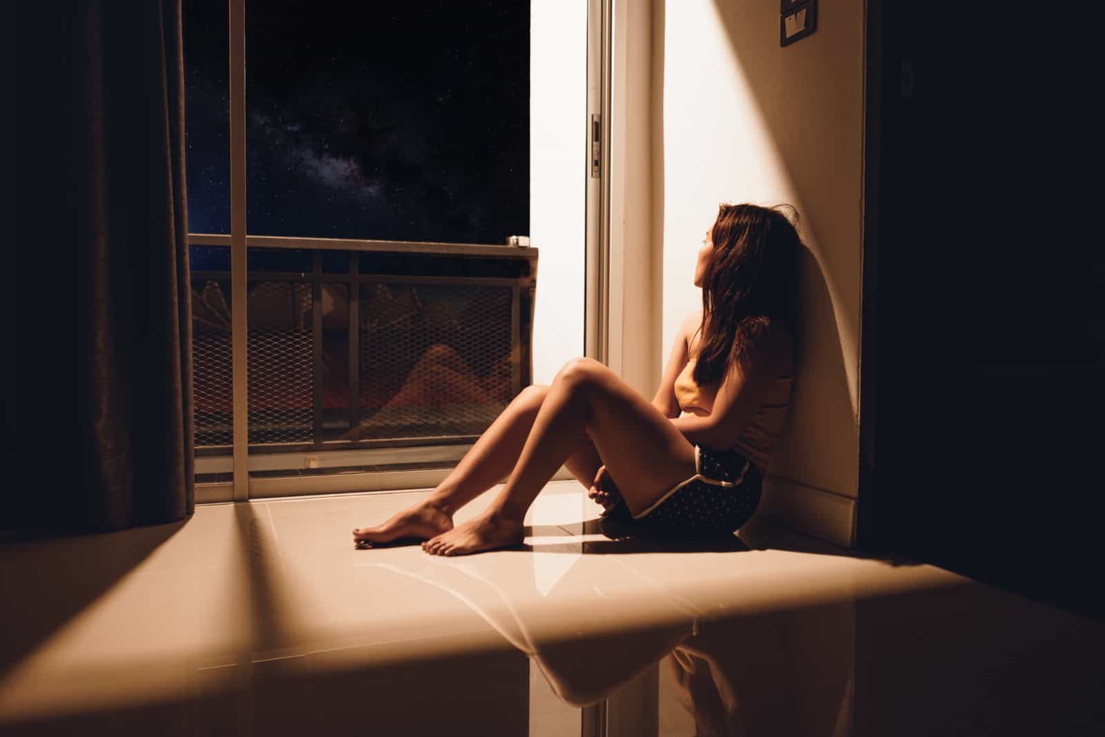 Sorgligt och deprimerat sammanträde för ung kvinna på golvet