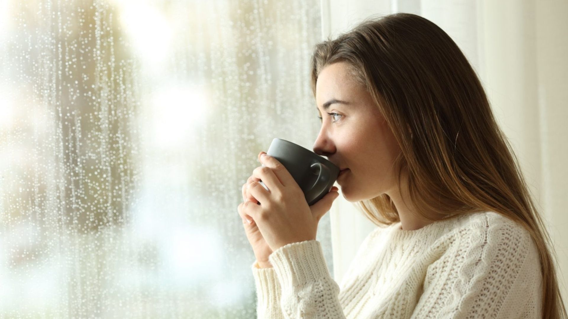 kvinna dricka kaffe tittar utanfoer genom ett foenster