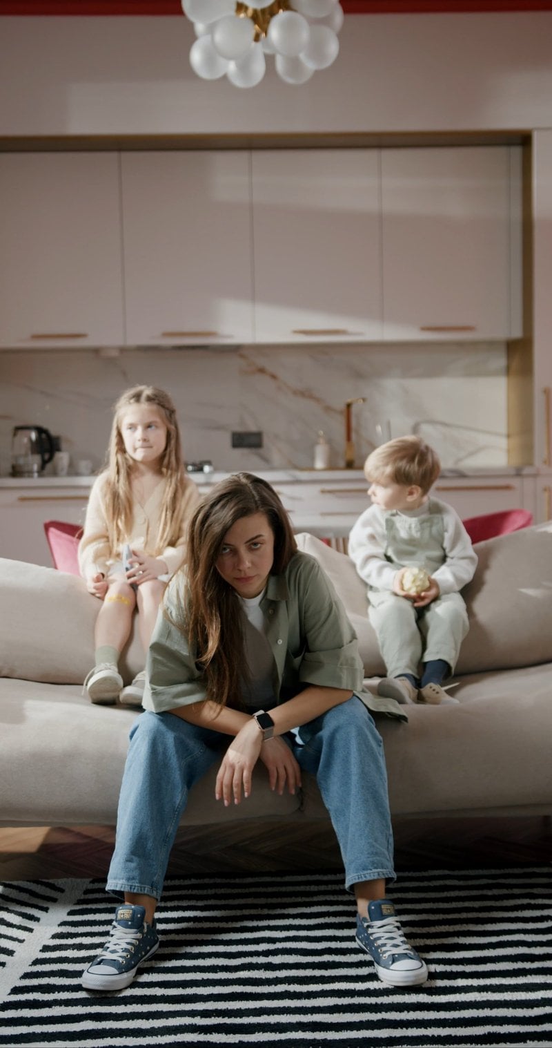 A Mother Feeling Tired While Sitting On Sofa With Her Children