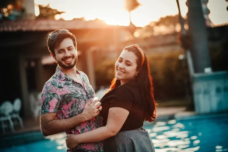 Ein Mann in einem Sommerhemd steht am Pool in den Armen einer dicken Frau