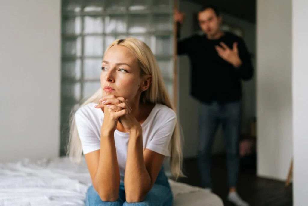 Ein Mann steht in der Tuer, waehrend eine Frau auf der Couch sitzt