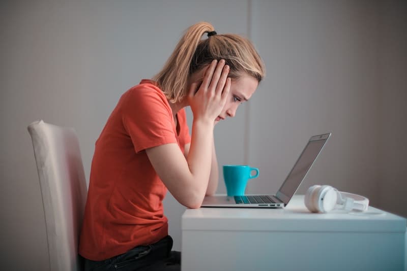 Eine ungl&uuml;ckliche junge Frau sitzt und schaut besorgt auf etwas auf ihrem Laptop