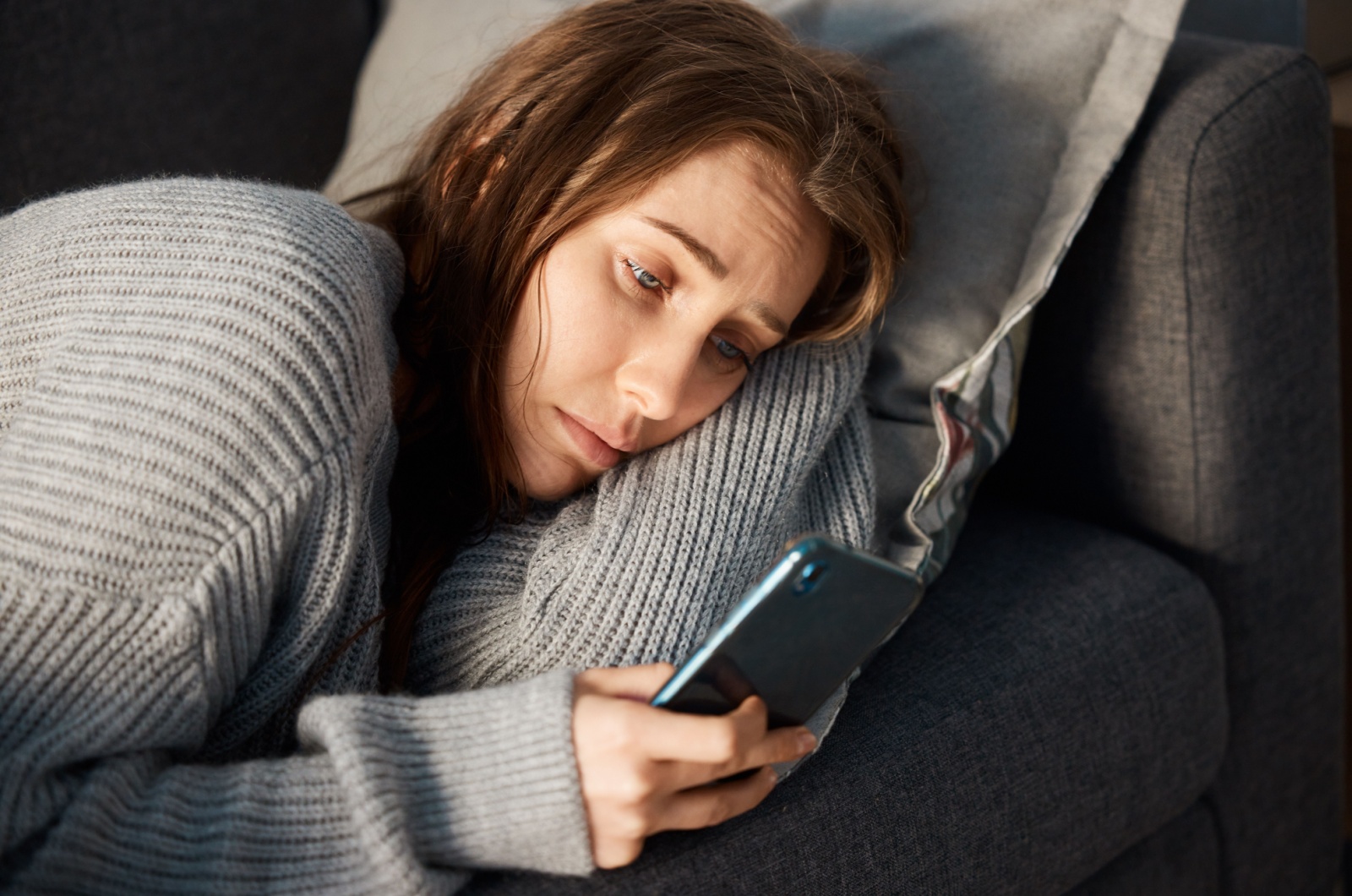 frau liegt traurig im bett mit handy in der hand